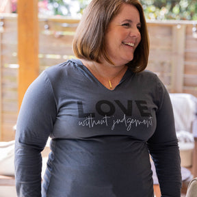 Woman wearing a gray long-sleeve shirt with 'LOVE without judgement' text outdoors.