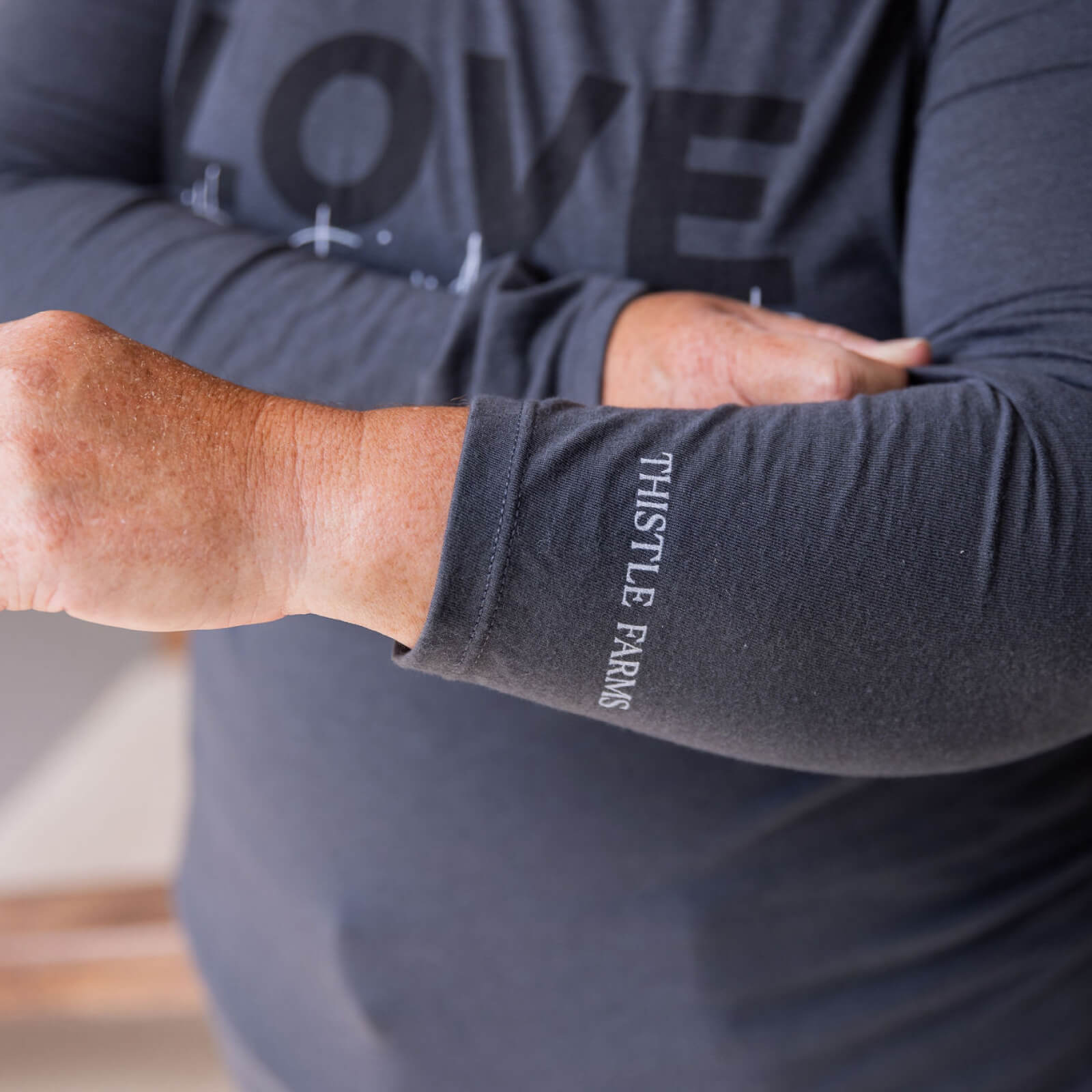 Person wearing a dark gray long-sleeve shirt with 'Thistle Farms' branding on the sleeve.
