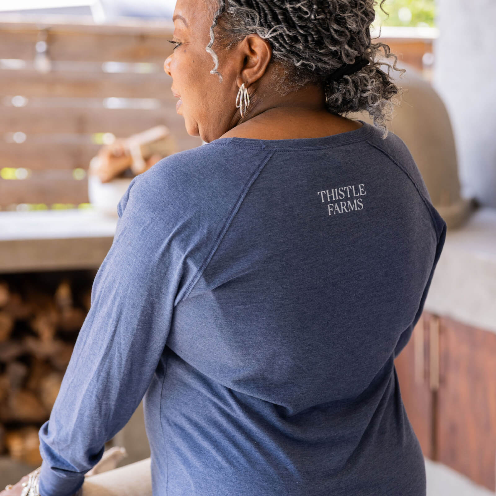 Person wearing a blue shirt with 'Thistle Farms' logo in an outdoor setting