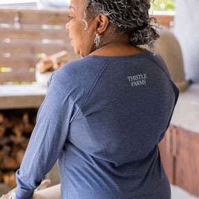 Person wearing a blue shirt with 'Thistle Farms' logo in an outdoor setting