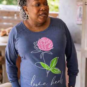 Woman wearing a blue sweatshirt with a pink rose, green leaves, and LOVE HEALS script 