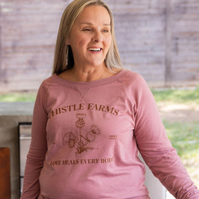 Woman wearing a pink long-sleeve shirt with 'Thistle Farms' branding and text.