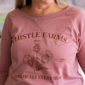 Pink sweatshirt with 'Thistle Farms' branding and floral design.