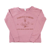Pink long-sleeve shirt with 'Thistle Farms' branding and text on a white background