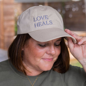 Person wearing a beige cap with 'LOVE HEALS' text, outdoors.