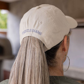 Person wearing a beige cap with 'Thistle Farms' logo, blurred background