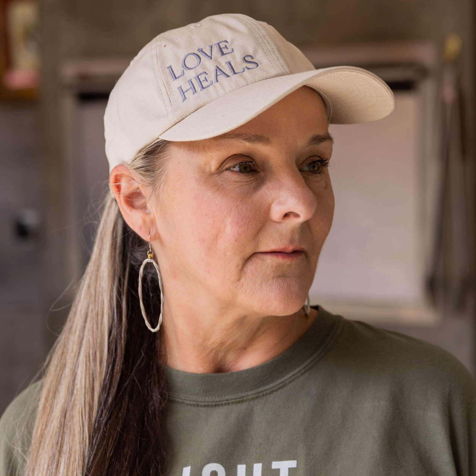 Woman wearing a cap with 'LOVE HEALS' text in a kitchen setting