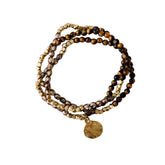Stack of brown and gold beaded bracelets with a gold charm on a white background