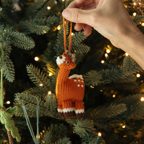 Hand holding a knitted deer ornament against a Christmas tree background