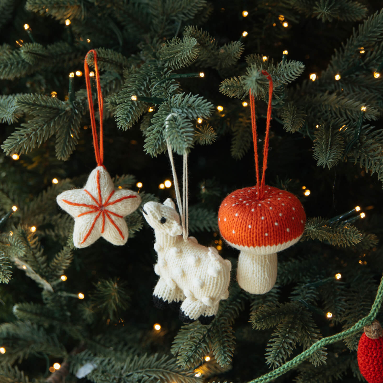 Knitted Christmas ornaments on a decorated tree with lights.