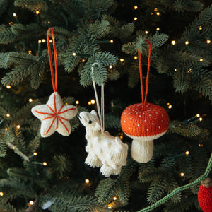 Knitted Christmas ornaments on a decorated tree with lights.