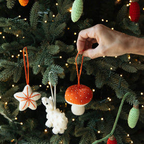 Hand selecting a knitted Christmas ornament from a decorated tree.