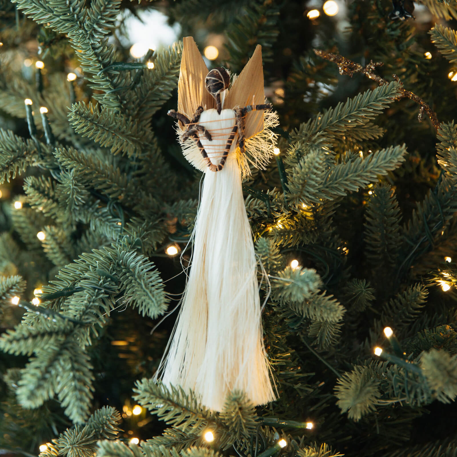 Decorative angel ornament on a Christmas tree with lights in the background