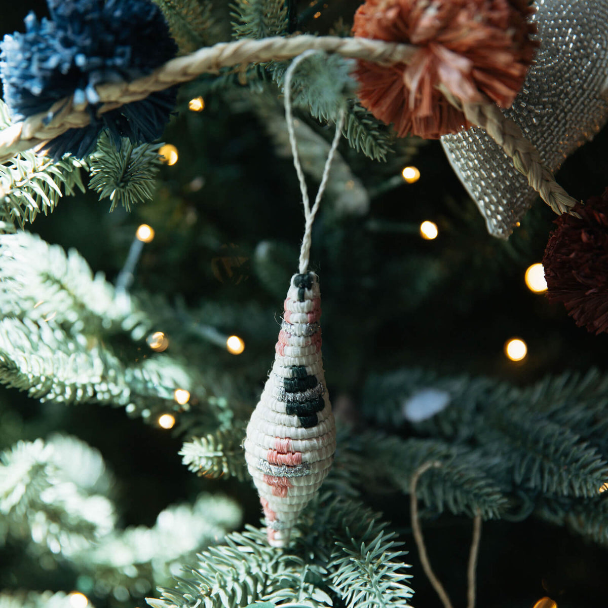 Decorative ornament hanging on a Christmas tree with lights in the background
