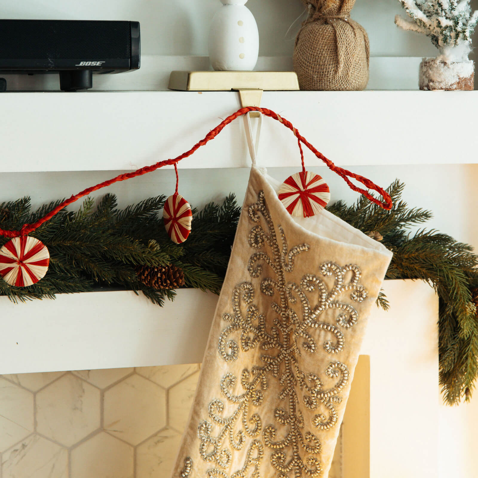 Decorative beige stocking with gold embellishments hanging on a mantel with Christmas decorations.