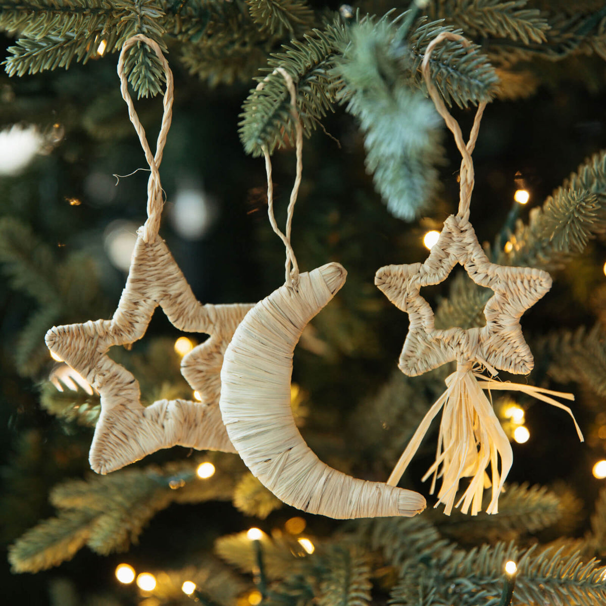 Decorative star and moon ornaments hanging on a Christmas tree with lights.