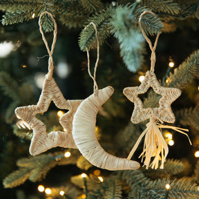 Decorative star and moon ornaments hanging on a Christmas tree with lights.