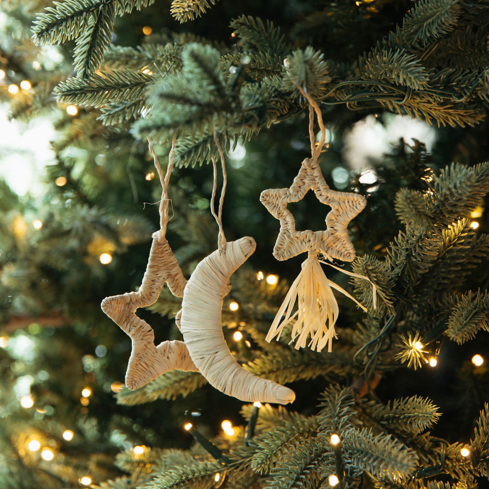 Decorative star and moon ornaments on a Christmas tree with twinkling lights.