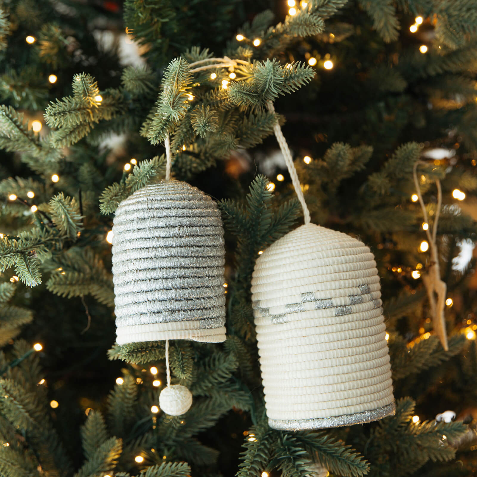 Two textured bell-shaped ornaments hanging on a decorated Christmas tree.