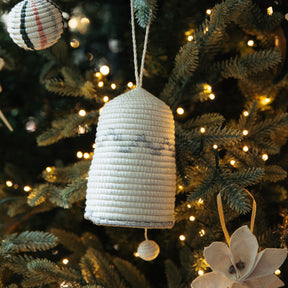 Textured bell ornament hanging on a decorated Christmas tree with lights.