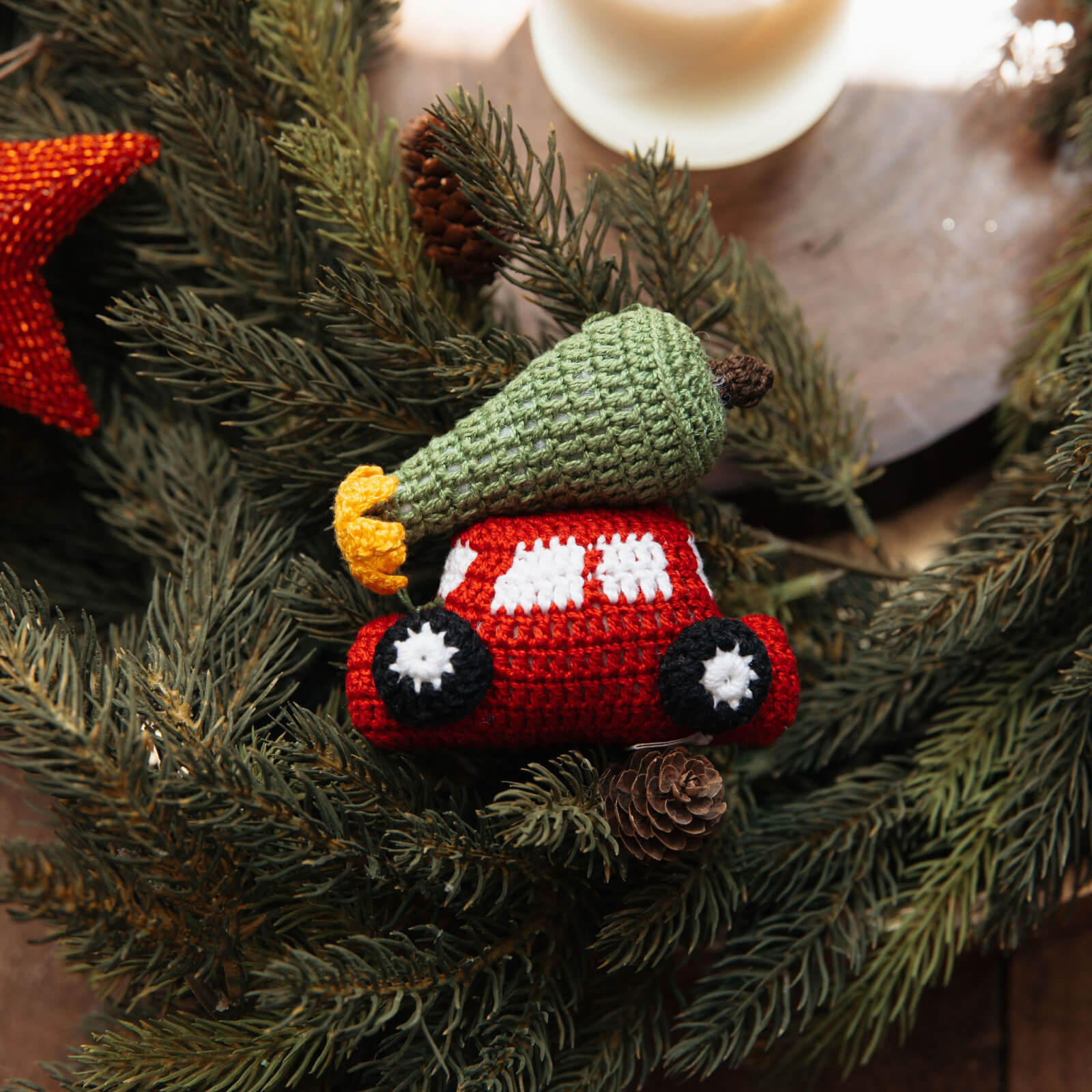 Crocheted red car ornament with a green tree on top, hanging on a Christmas wreath.