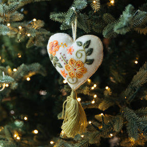 Heart-shaped embroidered ornament hanging on a decorated Christmas tree with lights.