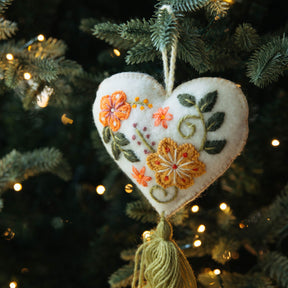 Decorative heart ornament with floral embroidery hanging on a Christmas tree.