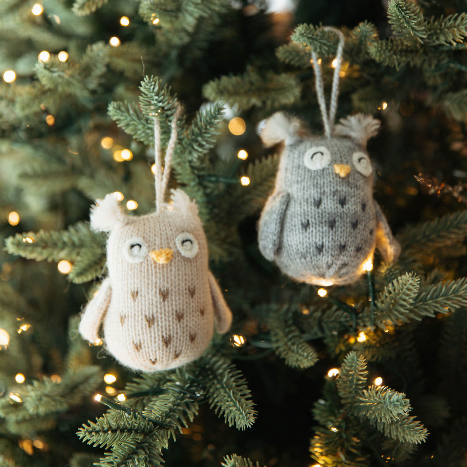 Two knitted owl ornaments hanging on a decorated Christmas tree.