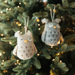 Two knitted owl ornaments hanging on a decorated Christmas tree.