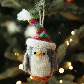 Knitted penguin ornament with a colorful hat hanging on a Christmas tree.