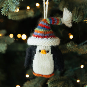 Knitted penguin ornament with a colorful hat hanging on a Christmas tree.