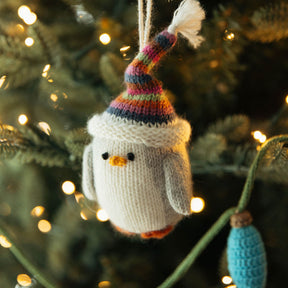 Knitted penguin ornament with a colorful hat hanging on a Christmas tree.