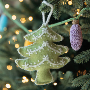 Green tree-shaped ornament with white snowflake details hanging on a Christmas tree with lights.