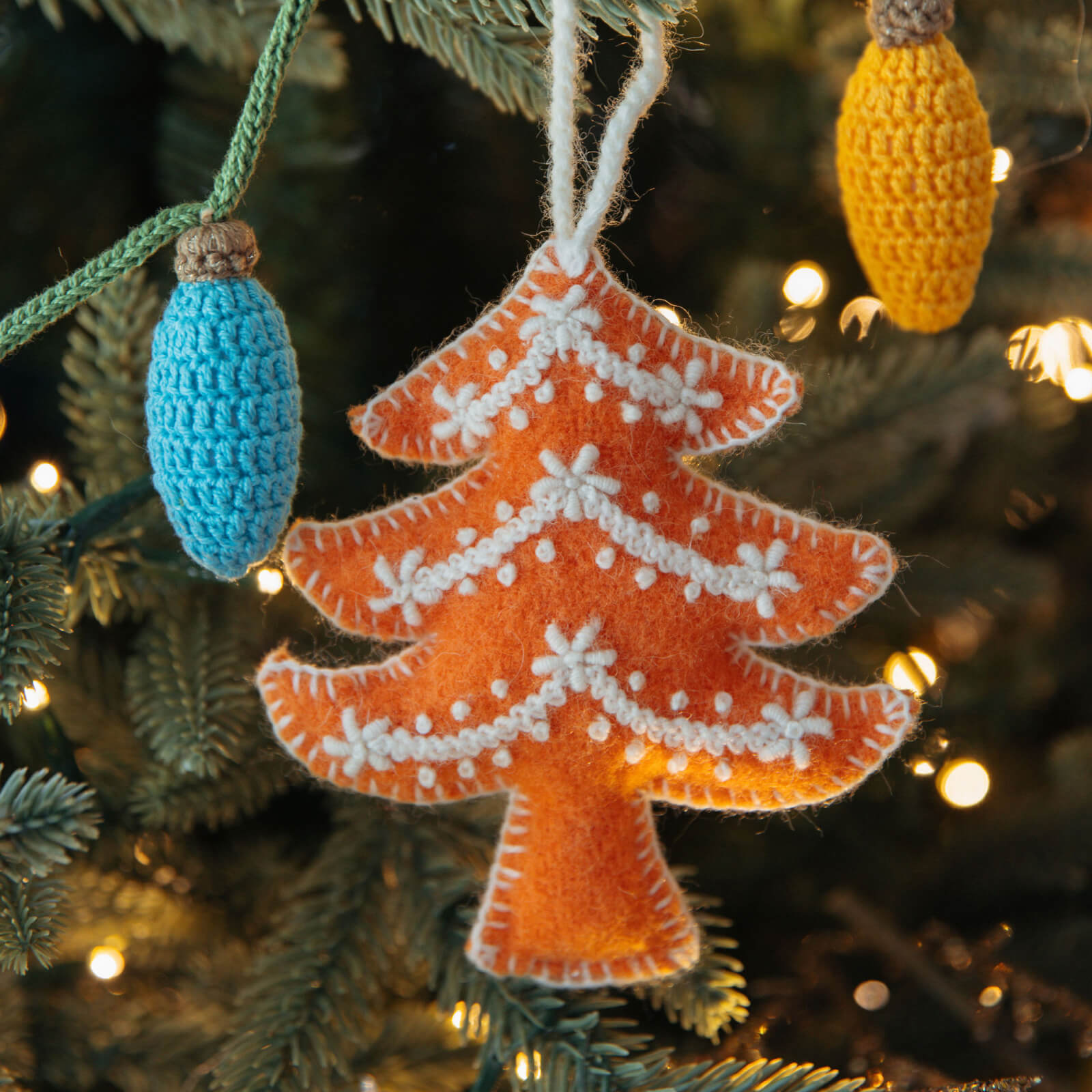 Orange Christmas tree ornament hanging on a lit Christmas tree.
