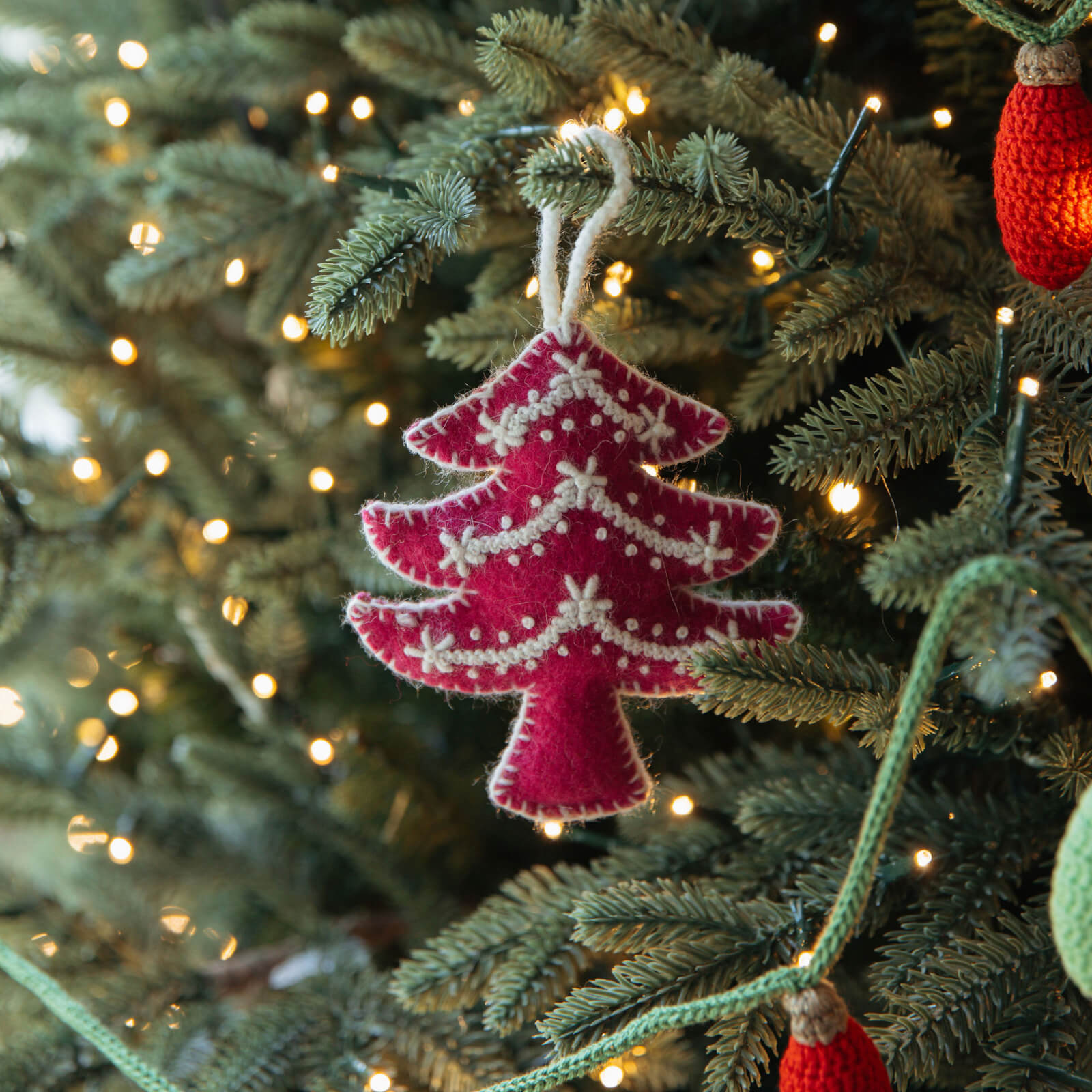 Pink knitted Christmas tree ornament on a decorated tree with lights.