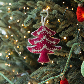 Pink knitted Christmas tree ornament on a decorated tree with lights.