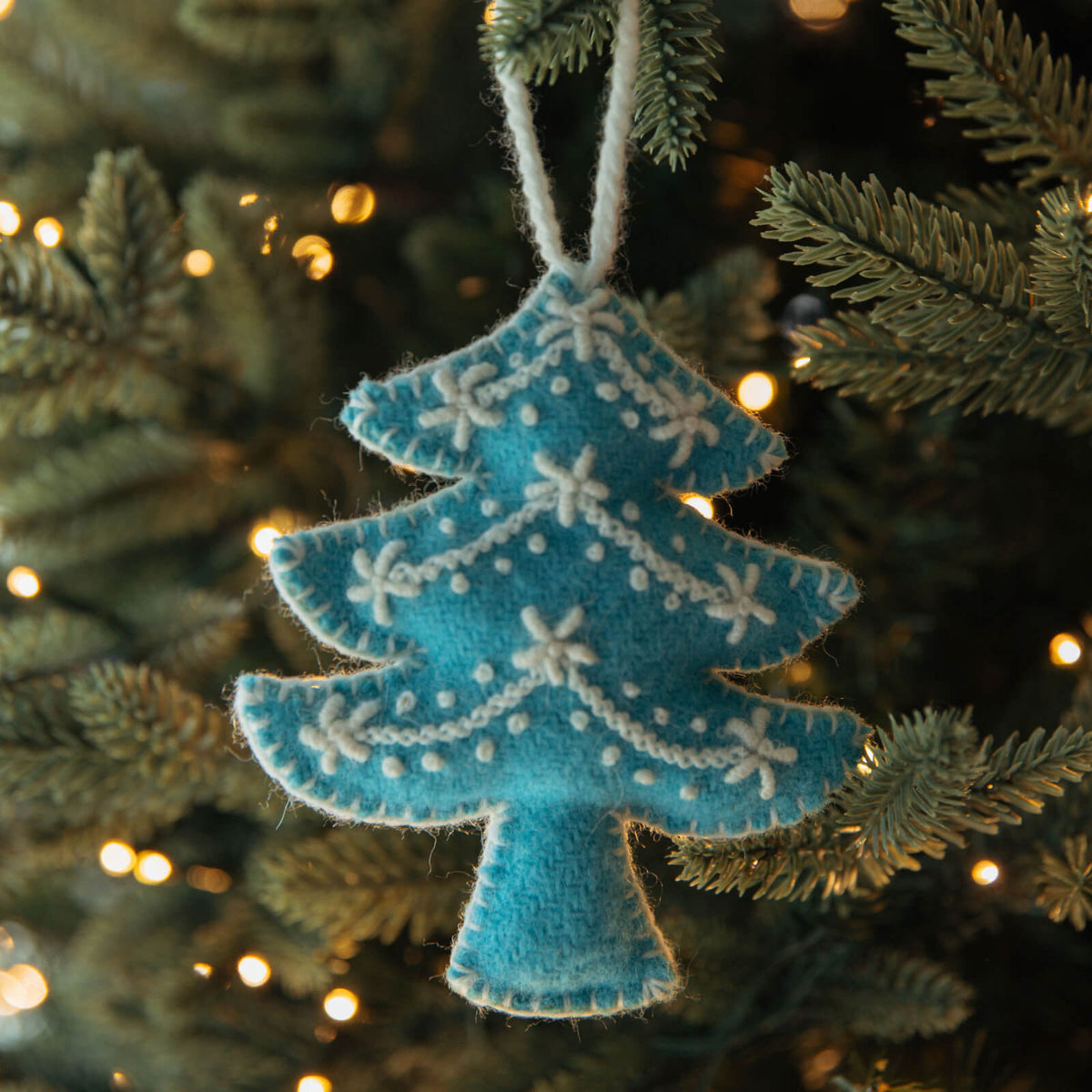 Blue felt Christmas tree ornament on a decorated tree with lights.