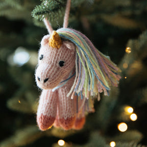 Knitted unicorn ornament hanging on a Christmas tree with blurred lights in the background