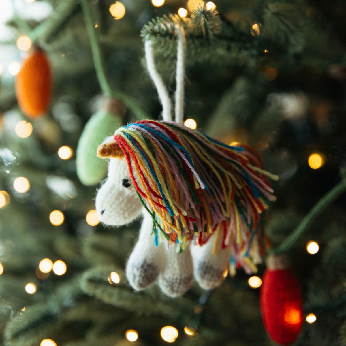 Knitted unicorn ornament with colorful mane hanging on a Christmas tree.