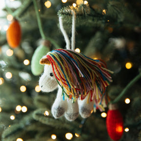 Knitted unicorn ornament with colorful mane hanging on a Christmas tree.