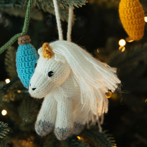 Knitted unicorn ornament hanging on a Christmas tree with blurred lights in the background