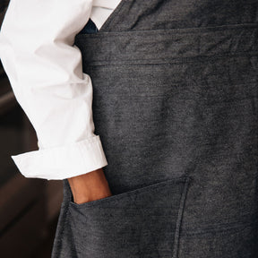 Close-up of a person wearing a dark gray apron over a white shirt.