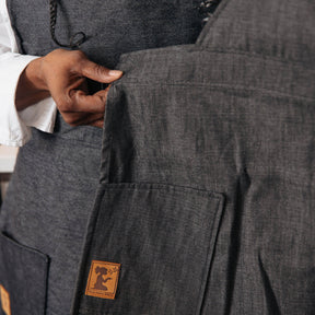 Close-up of dark gray pants with a brand logo on the pocket, worn by a person.