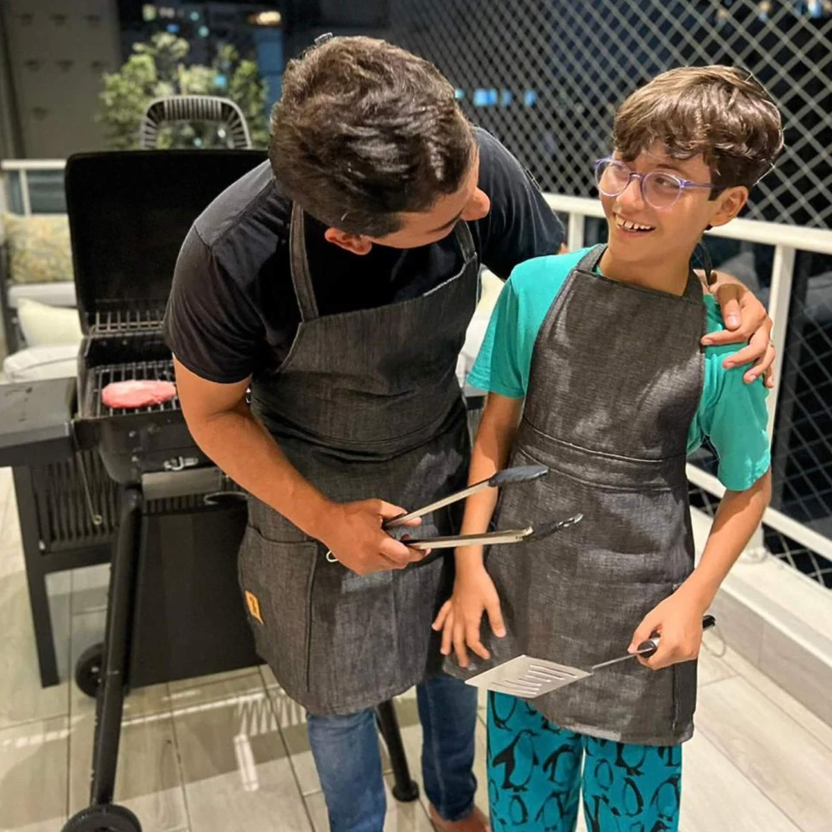 Two people wearing aprons standing next to a grill outdoors.