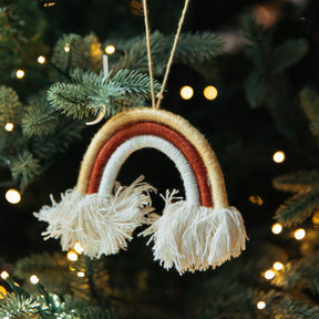 Decorative rainbow ornament with tassels hanging on a Christmas tree.