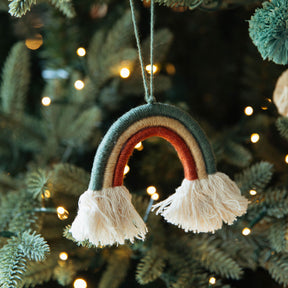 Decorative rainbow ornament with tassels hanging on a Christmas tree.