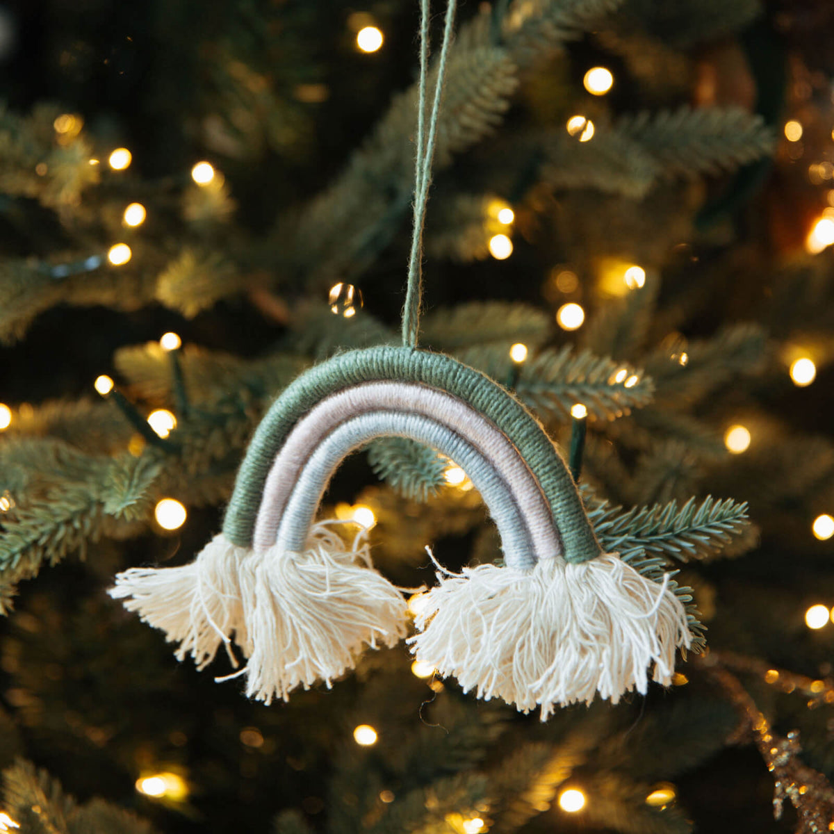 Decorative rainbow ornament with tassels hanging on a Christmas tree.