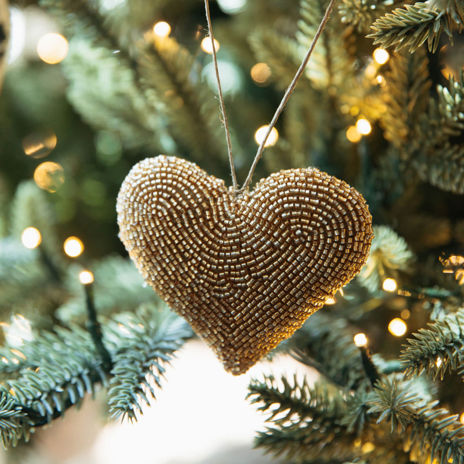 Heart-shaped beaded ornament hanging on a Christmas tree with lights in the background