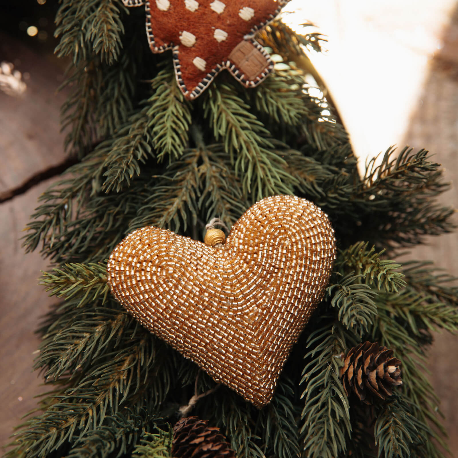 Gold beaded heart ornament on a Christmas tree with pine cones and lights.