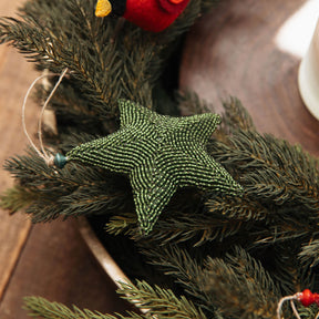 Green beaded star ornament on a Christmas wreath with red berries on a wooden surface.